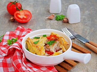 Fish fillet baked with tomatoes and garlic in a lavash bread envelope in a white portioned frying pan on a gray concrete background. Fish recipes.