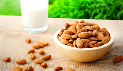Almond nuts with glass of almond milk on wooden table and linen cloth. Almonds in wooden bowl.