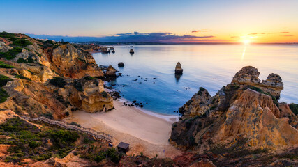 Obraz premium Sunrise at Camilo beach in Lagos, Algarve, Portugal. Wooden footbridge to the beach Praia do Camilo, Portugal. Picturesque view of Praia do Camilo beach in Lagos, Algarve region, Portugal.