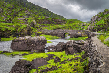Small stone Wishing Bridge over winding stream in green valley, Gap of Dunloe in Black Valley, Ring...