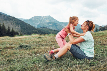 Little girl playing with her mother on grass enjoying summer day. Happy family playing in the field during vacation trip in mountains