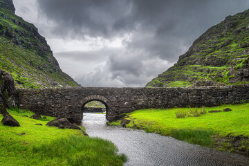 Small stone Wishing Bridge over winding stream in green valley, Gap of Dunloe in Black Valley, Ring of Kerry, County Kerry, Ireland