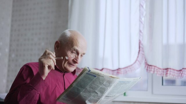 Tired old man touching sick eyes with hand and reading newspaper in room