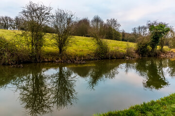 Fototapeta na wymiar Trees lining the Grand Union Canal near Foxton Locks, UK are reflected in the water on a still winter's afternoon