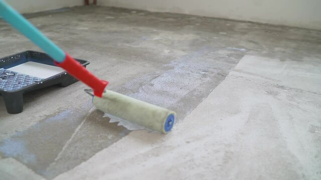 Roller with concrete floor mortar. Contract painter painting garage floor to speed up selling of home. Rolling Epoxy Paint on Concrete Floor. House under construction. Worker puts primer on concrete f