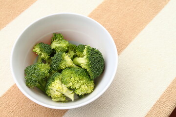 Healthy Broccoli flowers inside a bowl and on pastel colored kitchen cloth, Detail of healthy vegetarian food