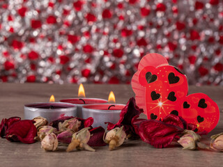 three candles that are burning and a heart behind rose petals on a table