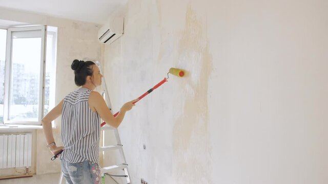A woman uses a roller to apply glue to the wall for subsequent wallpapering.