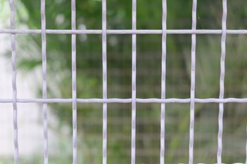 In selective focus a metal grey cage with grid pattern and blurred green nature background for a  backdrop,bokeh day light