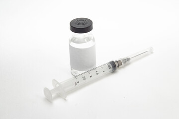 Vidro de vacina e seringa sobre a superfície branca de uma mesa.