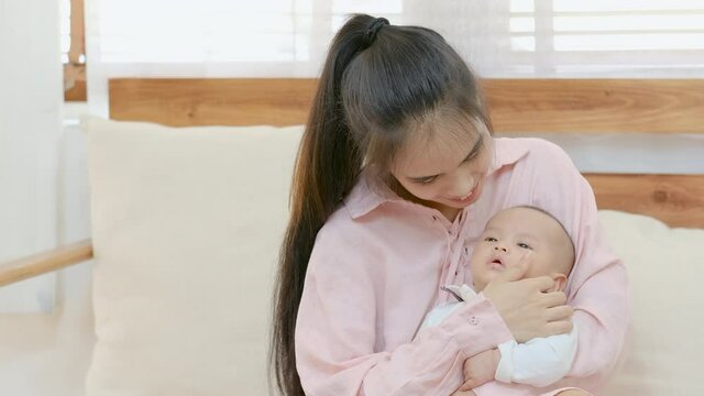 Young Asian mother enjoin to play and stay with her newborn baby in living room at home. She express love and care action to the baby with learning and healthcare support for kid in family concept.