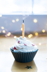 Birthday mini cake, muffin, cup cake with blown out candle. Muffin with cream and sugar hearts. Bokeh defocused background with yellow lights.