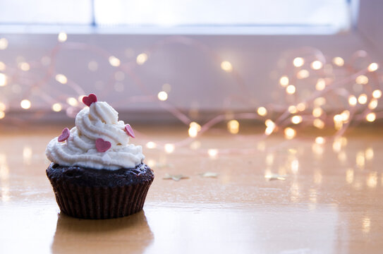 Cute muffin, with cream and sugar hearts. Bokeh, defocused background with yellow lights. Love, romantic cup cake for Valentine's day
