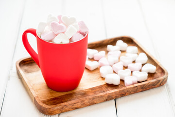 Red cup of hot cocoa with heart shaped marshmallows on white wooden background.