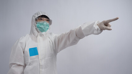 Doctor Gesture. Asian woman doctor in PPE suit or Personal Protection Equipment gesturing and point out. white medical rubber gloves. goggles glasses and green N95 mask to protect pandemic coronavirus