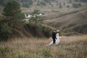 Obraz premium Romantic, young and happy caucasian couple in wedding clothes on the background of beautiful nature. Love, relationships, romance, happiness concept. Bride and groom traveling together.