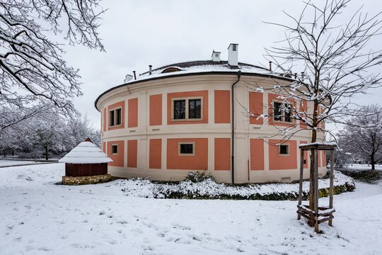 Prague, Czech Republic - January 7 2021: The Chodov fortress with red and pink facade standing in a park. Cloudy winter day with white snow covering ground and trees.