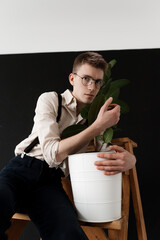 Young guy in round glasses and beige shirt hugs a tree in a white pot, ecology protection concept