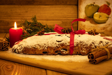 Traditional Christmas-stollen. He is lying on the board tied with a red ribbon. A candle burns nearby. A wooden table in the background is a wall of logs. The photo shows the real spirit of Christmas.