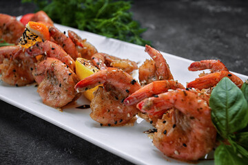 Fried shrimps in garlic-soy sauce, with sesame seeds, on a white plate, on a dark background