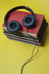 on a yellow background are a stack of books and large, black headphones.