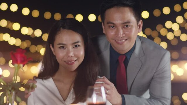 Young asian couple take photo for memory of happiness moment at romantic dinner in rooftop restaurant at city night with sweet moment celebrate anniversary. Love relationship, marry concept.