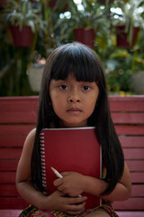 Pretty little girl holding a book and pencil and sitting in the backyard 