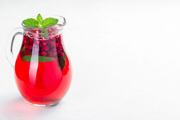 Punch or limeade with lingonberry and lime in a glass pitcher on gray background, horizontal, copy space