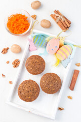 Homemade carrot cake and walnut muffins on wooden tray with Easter eggs, bunnies and feathers, vertical, top view