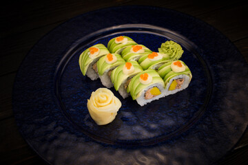 Side view of Japanese sushi roll with avocado slices and red caviar on top served with ginger and...