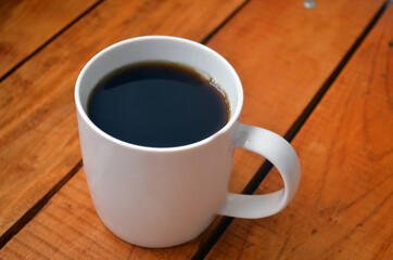 White cup with coffee on a wooden background.