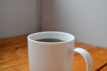 White cup with coffee on a wooden background.