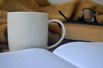 White mug with coffee and steam on a brown plaid, book, notebook