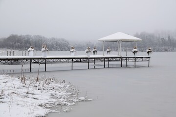 Beautiful winter on Lake Otominskie in misty scenery, Kashubia, Poland. Wooden pier with white...