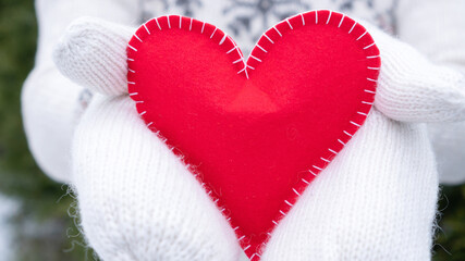 Red heart close up as a concept of declaration of love for Valentine's Day. A woman in white woolen mittens holds out her heart to her beloved. Red heart for Valentine's Day greeting card.