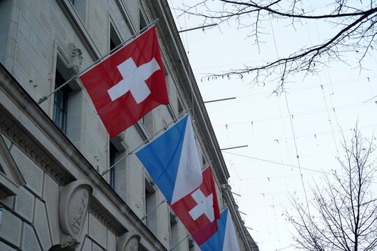 Detail of a Swiss federal flag and flag of canton Zurich displayed on the facade of a historic building in the city center of Zurich. Low angle view.
