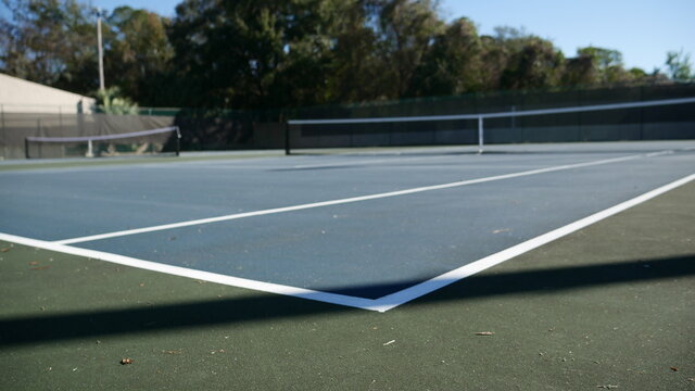 Low angle corner view of an empty tennis court with lamp post shadow