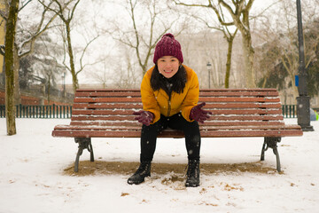 lifestyle portrait of young happy and attractive Asian Korean woman in Winter jacket and beanie enjoying snowfall at city park playing with snow cheerful during Christmas holidays