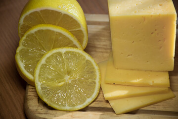 Sliced ​​cheese and lemons on a wooden board.