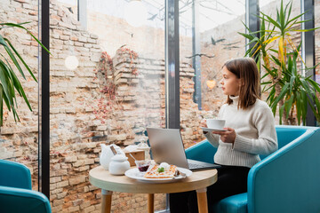 Girl with a cup and laptop at a table in a cafe.