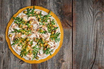 Delicious raw pizza with mushrooms, walnuts, arugula and green olives. Top view.