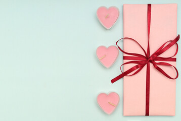 Beautifully packaged pink gift box with red ribbon and pink heart-shaped candles on a blue background. Concept of Valentine's day gifts. The view from the top.Copy space