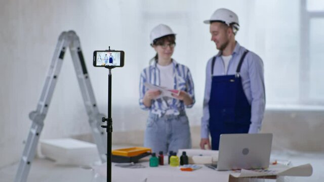 renovation blog, young cheerful man and woman talk about new wall painting and show color scheme and paint roller in phone camera while recording video for social networks on smartphone