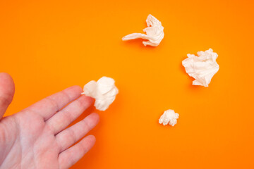 the hand drops the crumpled napkin next to the other crumpled napkins. orange background