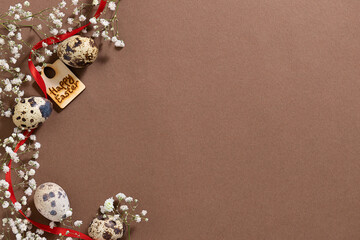 Minimalism style Easter background with beautiful white spring flowers, quail eggs, wooden decorations and red ribbon on natural brown background. Zero waste eco friendly Easter decorations concept.