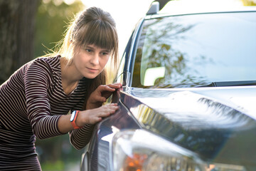 Young woman customer closely examining a new car at dealer outdoor shop before purchasing it.