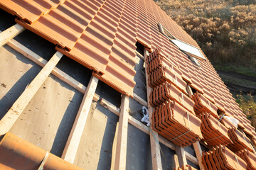 Stacks of yellow ceramic roofing tiles for covering residential building roof under construction. - obrazy, fototapety, plakaty
