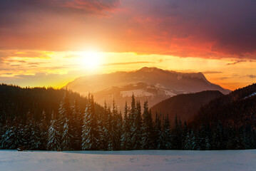Winter landscape with high peaks and foggy valley under vibrant colorful sunset evening sky in rocky mountains.