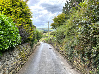 Fototapeta na wymiar Looking down, Bents Lane, with stone walls, wild plants, and a cloudy sky in, Queensbury, Bradford, UK