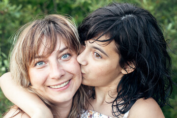 Portrait of happy woman kissing her daughter, outdoors.
